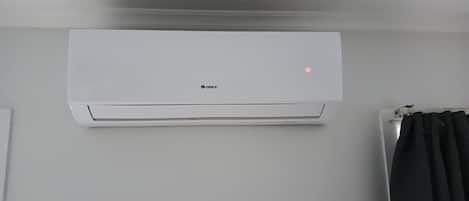 A white GREE air conditioning unit mounted on a wall in a room with a plain white wall and a black curtain.