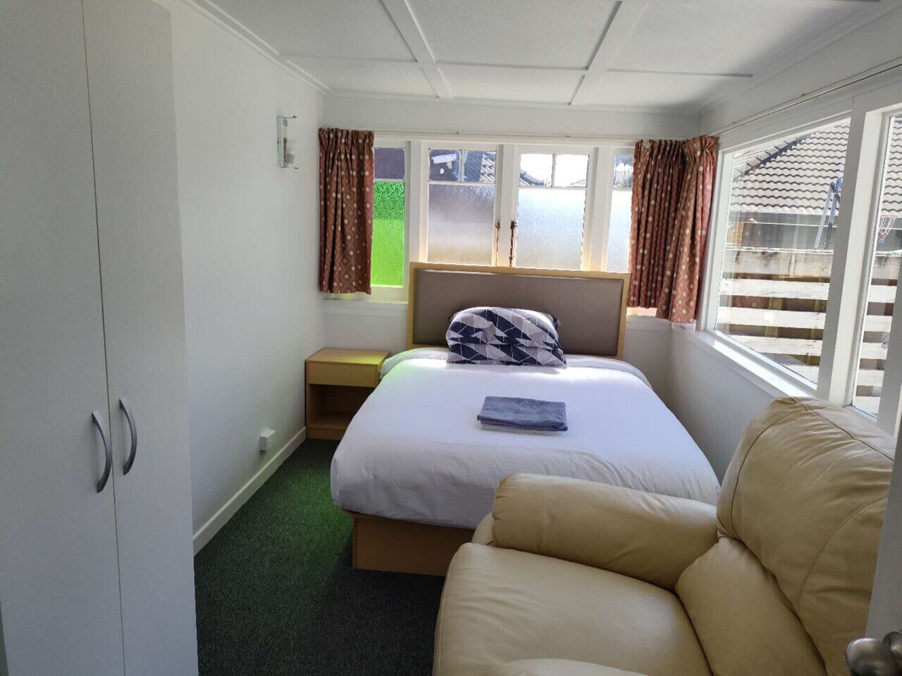 Une chambre à coucher comprenant un lit, une table de chevet, une armoire et une fenêtre avec des rideaux.