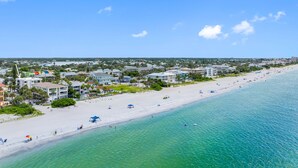 A coastal resort with a wide sandy beach, clear turquoise waters, and a backdrop of residential buildings.