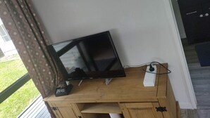 A television on a wooden stand in a room with a window and a door leading to a kitchen. - 2 double beds including 1 double sofa bed Garden Chalet, 7 Rangiatea Road, Epsom, Auckland (Auckland)