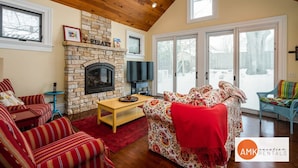 A cozy living room with a stone fireplace, a television, and a large window.