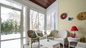 A cozy room with wicker furniture, large windows, and a view of trees.