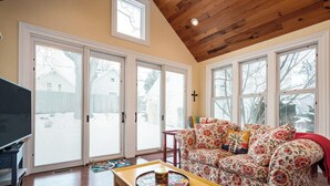 A living room with a wooden ceiling, large windows, a sofa, a coffee table, and a television.