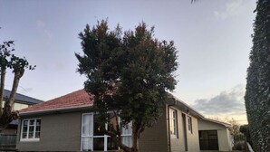 Une maison à deux étages, avec un toit recouvert de tuiles rouges, un petit porche à l’avant et un arbre devant.