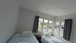 Une petite chambre propre, avec deux lits simples, une fenêtre avec des rideaux et une vue sur l’extérieur.