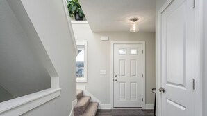 A modern interior with a staircase, a white door, and a ceiling light fixture. - Deer Haven in Georgetown Township (Jenison)