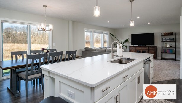 A spacious kitchen with a large island, modern pendant lights, and a view of the outdoors. - Deer Haven in Georgetown Township (Jenison)