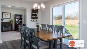 A dining area with a wooden table, six chairs, a chandelier, a fireplace, a bookshelf, and a large window with a view of the outdoors. - Deer Haven in Georgetown Township (Jenison)