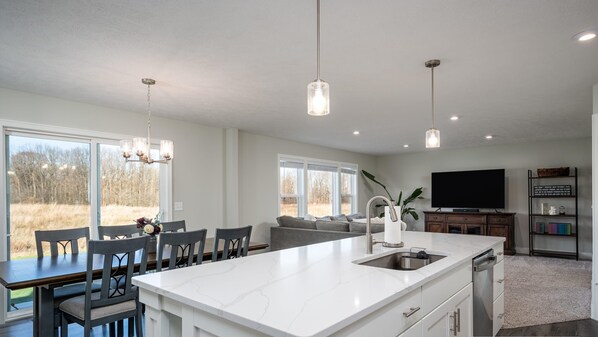 A spacious kitchen with a large island, modern pendant lights, and a view of the outdoors.