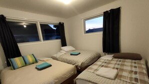 Een kamer met twee eenpersoonsbedden, elk voorzien van een kussen en een opgevouwen handdoek. Er zijn ramen met gordijnen, en de vloer is van hout.