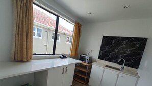 A compact kitchen with white cabinets, a window with curtains, a marble backsplash, and a small countertop with a toaster. - 6 Beds including 4 Double Beds and 2 Sofa Bed Garden Chalet, 8 Renton Road, Mt Albert, Auckland (Auckland)