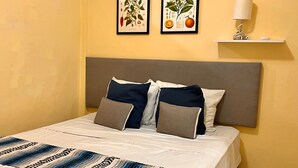 A neatly made bed with a patterned bedspread, a gray headboard, and two framed botanical prints on the wall. - 10 Coleguita in Isla Mujeres (Isla Mujeres)