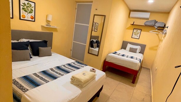 A hotel room with two beds, a mirror, a shelf with a lamp, and a wall-mounted air conditioner. - 10 Coleguita in Isla Mujeres (Isla Mujeres)