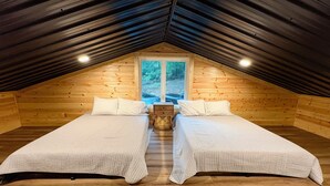 Un dormitorio acogedor en el ático con dos camas, paredes de madera y una ventana con vistas a árboles.