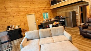 Una sala de estar acogedora con un sofá seccional, una zona de cocina y un balcón con barandilla.