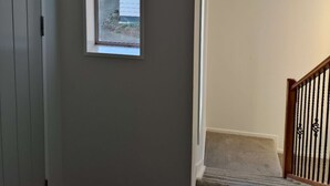 Un passadís amb una finestra, una porta i una escala amb barana.