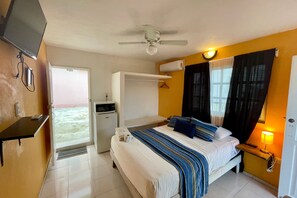 A hotel room with a bed, a desk, a ceiling fan, an air conditioning unit, and a view of the outside. - 07 Estudio in Isla Mujeres (Isla Mujeres)