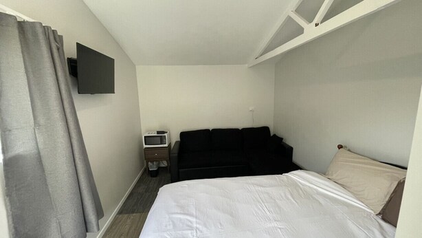 A hotel room with a bed, a black sofa, a TV mounted on the wall, and a microwave on a small table. - 3 Beds including 1 Double Bed, 2 Single Sofa Beds Garden Chalet, Unit C, 9 Steeles Lane (Rotorua)