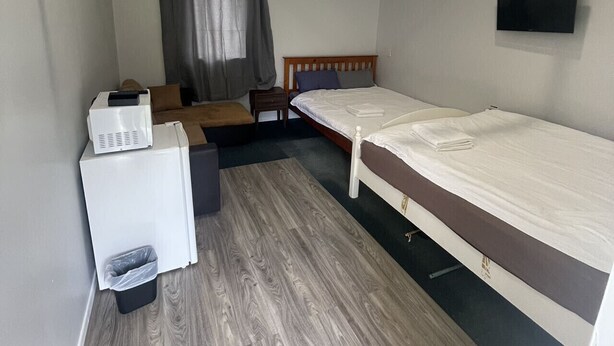 A compact room with a bed, a small desk, a chair, a TV, and a window with curtains. - 1 Double and 1 single Bed unit B (Rotorua)