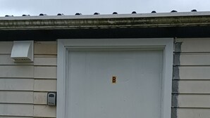 A white door with a small 'B' sign above it, set in a building with beige siding and a metal roof. - 1 Double and 1 single Bed unit B (Rotorua)