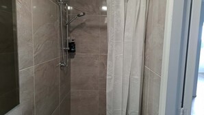 A shower with a handheld showerhead and a wall-mounted faucet, tiled walls, and a curtain.