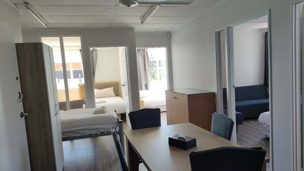 A compact hotel room with a bed, a desk, and a chair. There is a door leading to another room.