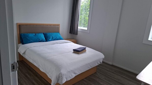A bedroom with a bed, a nightstand, a window with curtains, and a view of greenery outside. - 4 Bedrooms Apartment (Auckland)