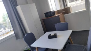 A small, neatly arranged room with a white table, four blue chairs, a black microwave on a wooden shelf, and a window with curtains. - 6 Beds including 1 DBL Bed, 1 Single Bed, 4 Singgle Sofa Bed in 1 Room & 1 Lounge (Auckland)