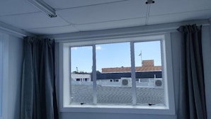 A room with a large window, curtains, and a view of a building with a flat roof and air conditioning units. - 6 Beds including 1 DBL Bed, 1 Single Bed, 4 Singgle Sofa Bed in 1 Room & 1 Lounge (Auckland)