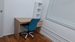 A corner office with a wooden desk, a teal office chair, and a white shelving unit. - 5 Beds including 1 Double Bed, 2 single Beds, 2 Double Sofa Beds, Suite 4 (Auckland)
