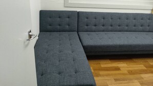 A gray sectional sofa in a room with wooden flooring and white walls. - 5 Beds including 1 Double Bed, 2 single Beds, 2 Double Sofa Beds, Suite 4 (Auckland)
