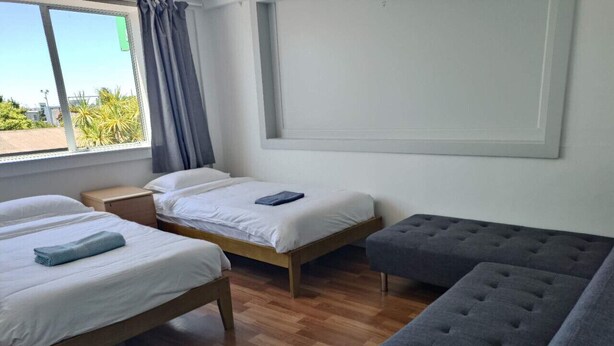A room with two single beds, a grey sofa, and a wooden floor. - 5 Beds including 1 Double Bed, 2 single Beds, 2 Double Sofa Beds, Suite 4 (Auckland)