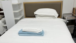 Uma cama bem arrumada com lençóis brancos, uma toalha azul dobrada e cabeceira de madeira.