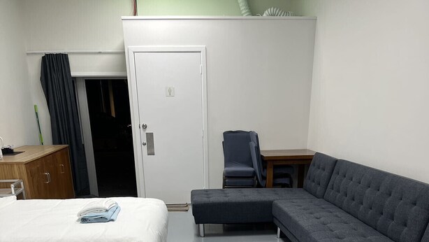 Um quarto com duas camas de solteiro, um sofá modular cinza, um armário de madeira e uma pequena mesa.