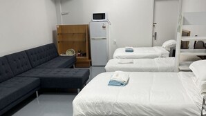 Quarto de hotel com sofá, duas camas de solteiro, um refrigerador e um armário de madeira.