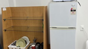 Uma cozinha compacta equipada com micro-ondas, frigorífico e um armário de madeira com louça e utensílios.