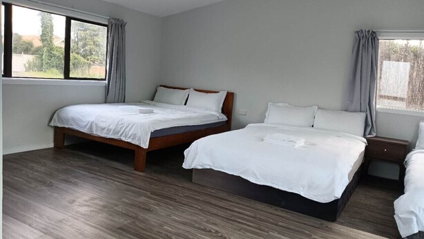 A bedroom with two beds, wooden flooring, and large windows with curtains. - 4 double and 2 Sofa Beds chalet (Rotorua)