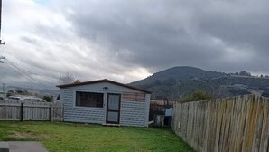 A small, single-story building with a sloped roof, a fenced yard, and a dirt path leading to it. - 4 double and 2 Sofa Beds chalet (Rotorua)