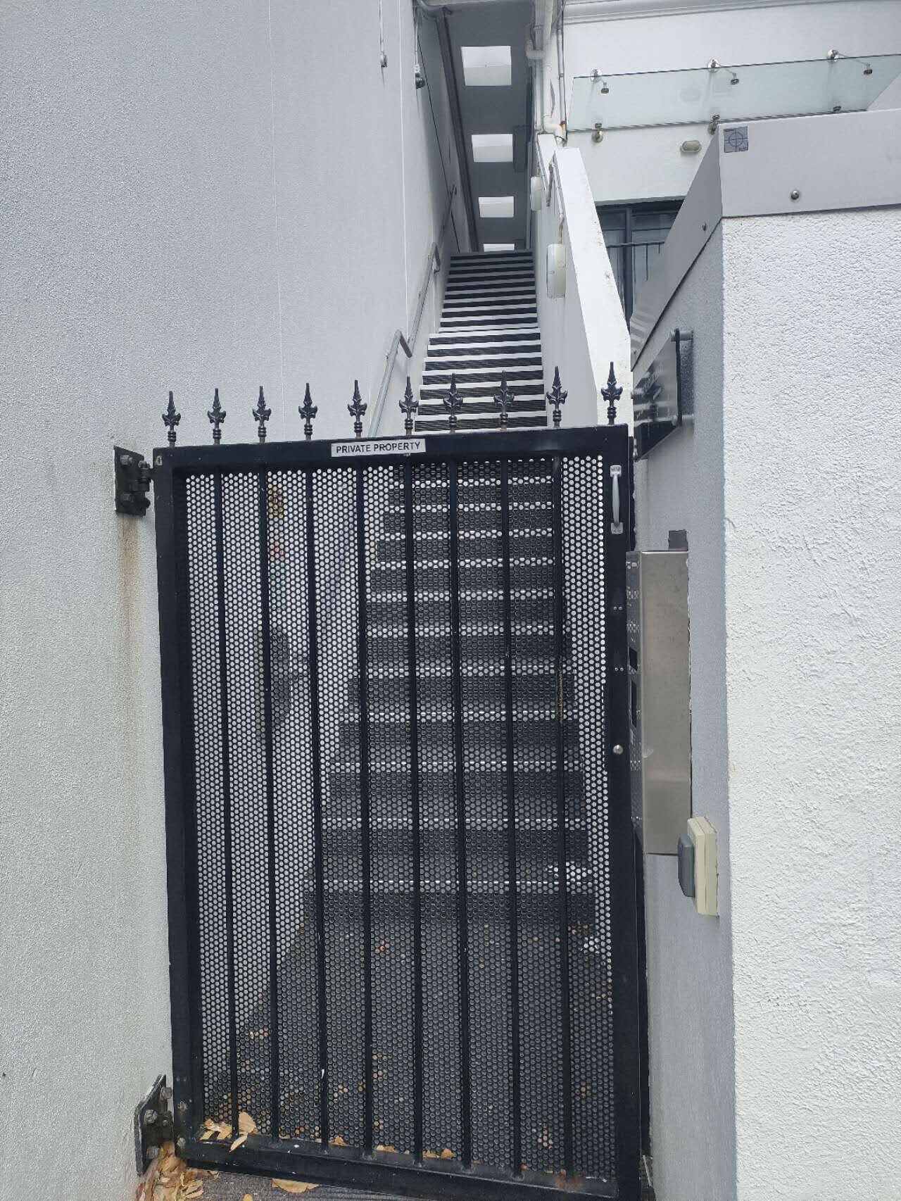 Una reja de metal negro con un letrero que dice “PROPIEDAD PRIVADA”, una pared blanca y una escalera que conduce a un nivel superior.