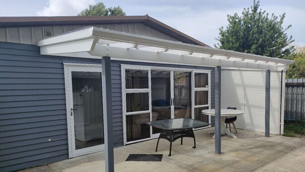 A covered patio area with a table and chairs, a sliding glass door, and a concrete floor. - 3 Bedroom Small House B (Auckland)