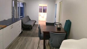 A compact room with a kitchenette, a dining table with chairs, a sofa, and a window with curtains. - 3 Bedroom Small House B (Auckland)