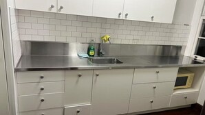 Keittiössä on valkoiset kaapit, ruostumattomasta teräksestä valmistettu työtaso ja mikroaaltouuni.