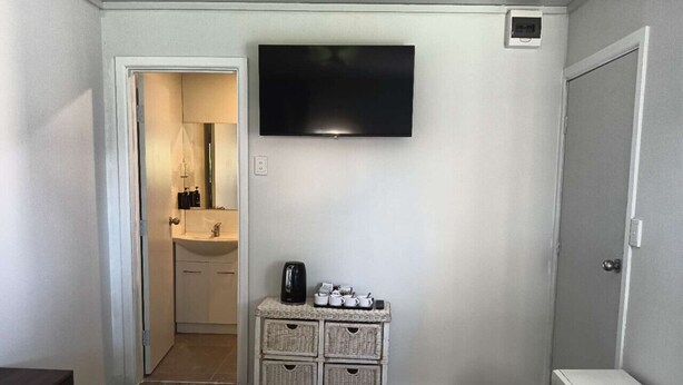 Habitación de hotel con cama, televisor montado en la pared, cómoda pequeña y microondas.