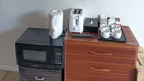 Una kitchenette con microondas, tostadora y cafetera sobre un mueble de madera, y un televisor de pantalla plana montado en la pared.