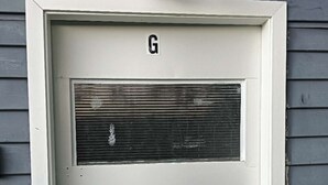 Une porte blanche, dotée d’une grille d’aération et d’une serrure, et portant la lettre « G ».