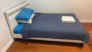 Ein Bett mit weißem Kopfteil, blauer Bettwäsche und einem weißen Handtuch am Fußende.