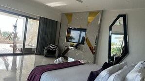 Une chambre d’hôtel moderne dotée d’un grand lit, d’un téléviseur fixé au mur et d’un balcon offrant une vue sur l’extérieur.