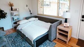 A neatly arranged bedroom with a bed, bedside table, lamp, and a small shelf with books and a sign. - Spacious & Cozy Home near Olde Town Arvada (Arvada)