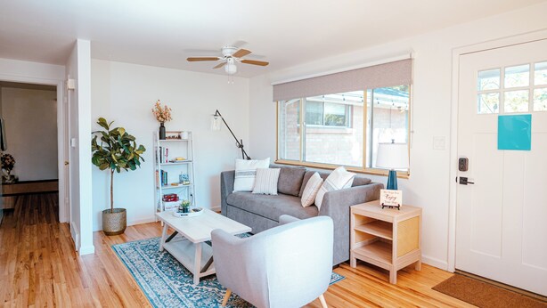 A modern living room with a grey sofa, white armchair, and a coffee table. There is a bookshelf, a potted plant, and a window with a view. - Spacious & Cozy Home near Olde Town Arvada (Arvada)
