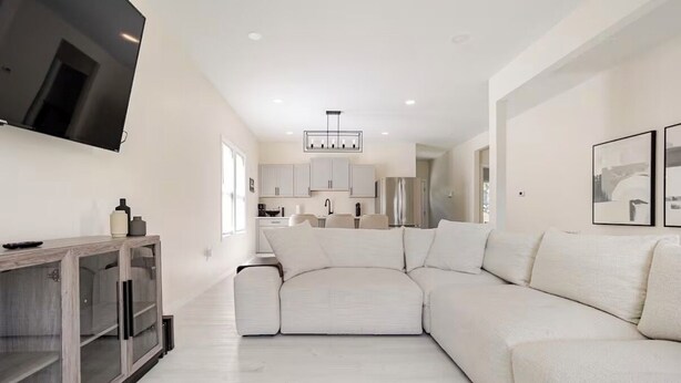 A modern living room with a large sectional sofa, a flat-screen TV mounted on the wall, and a minimalist kitchen in the background.